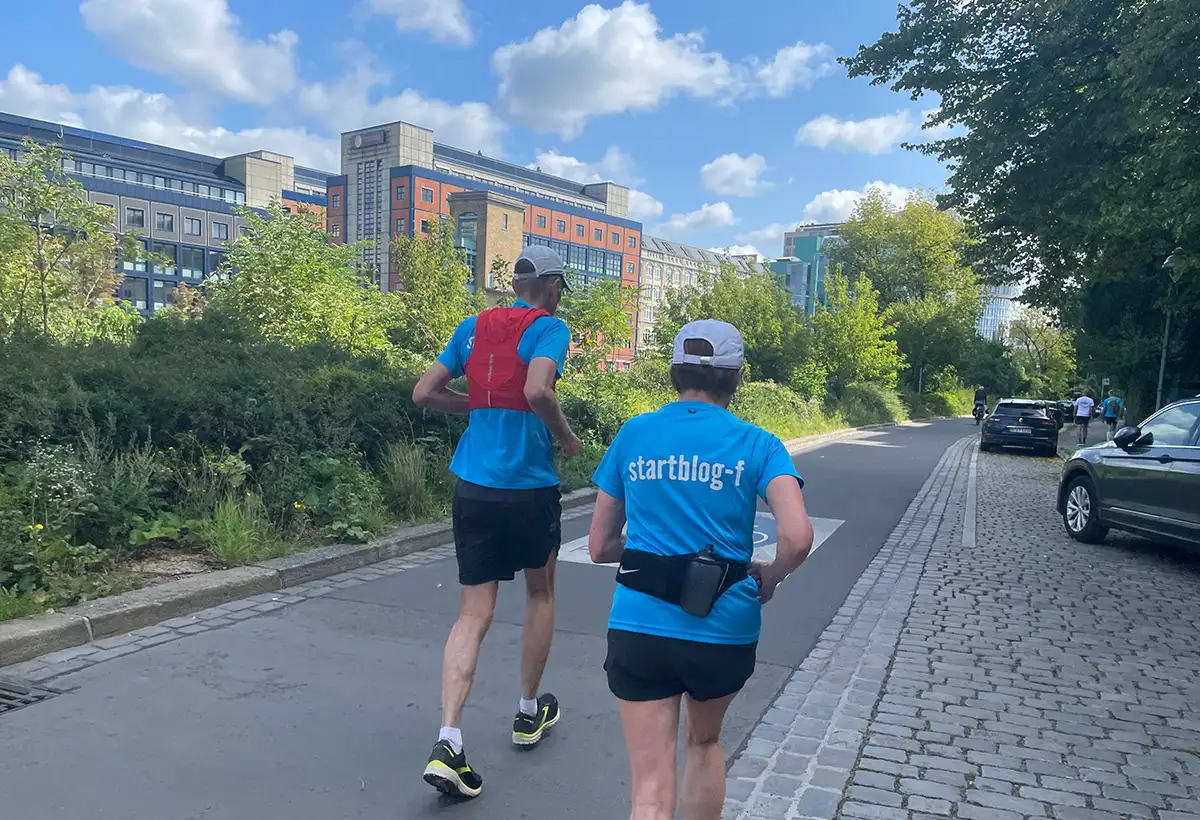 Läuferpaar auf einer schmalen Straße, im Hintergrund Gewerbegebäude am anderen Ufer der Spree