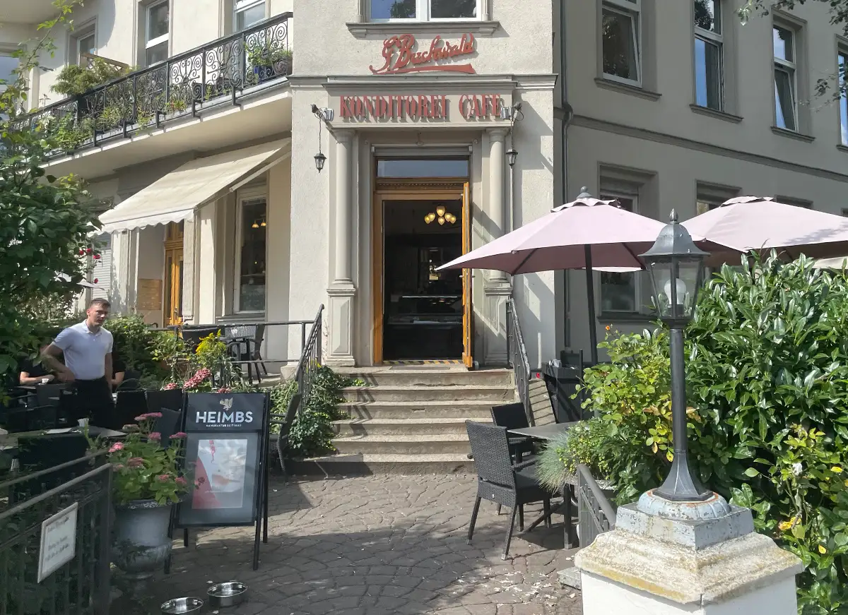 Eingangsbereich mit Vorgarten einer Konditorei mit Tischen und Sonnenschirmen