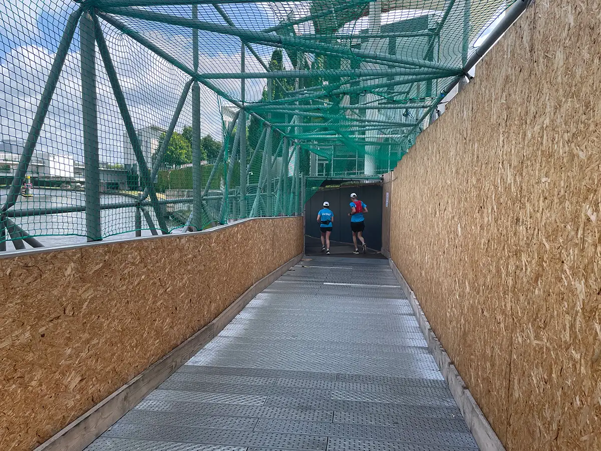 Läuferpaar in einem Baustellen-Tunnel, der oben mit einem grünem Netz abgedeckt ist