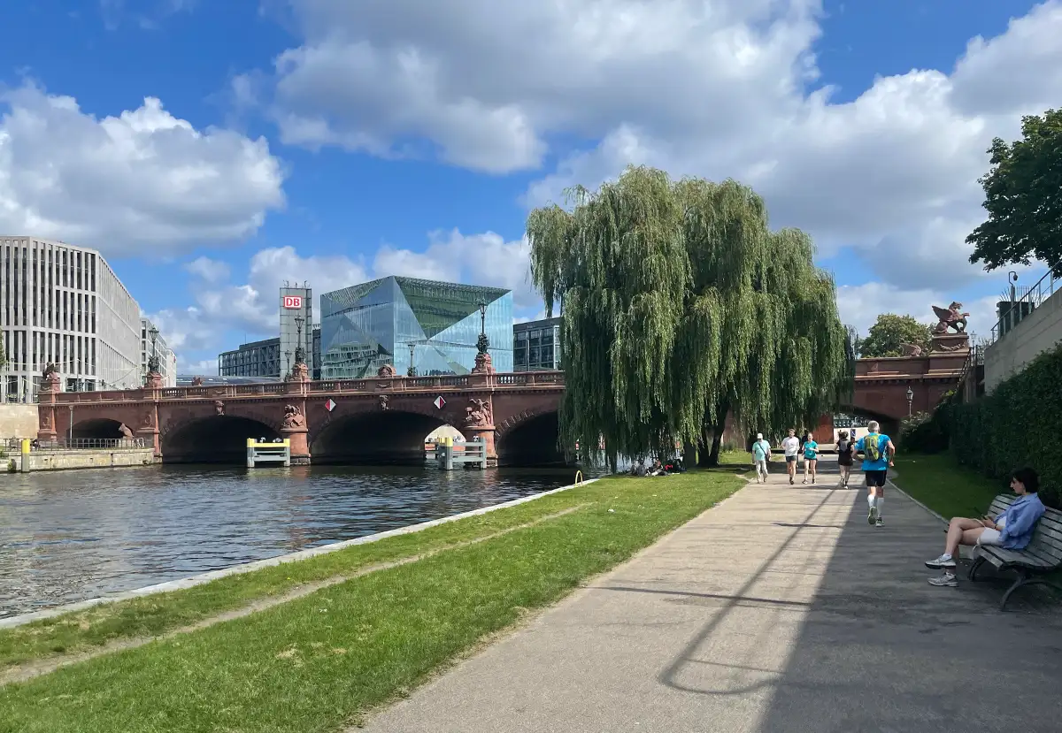 Läufer und Passanten auf der Uferpromenade an der Spree auf Höhe der Moltkebrücke hinter der Bürogebäude und der Hauptbahnhof zu sehen sind