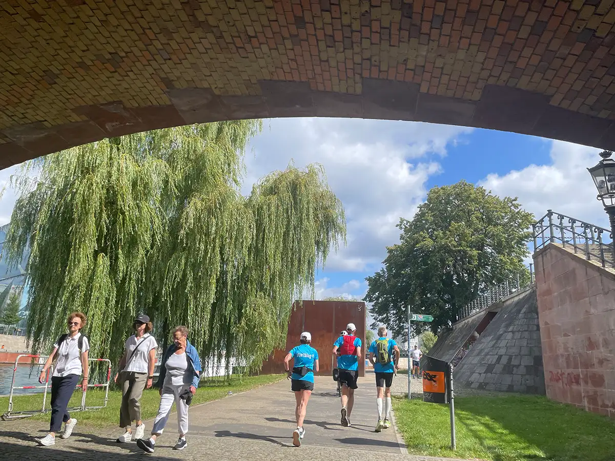 Läufer und Passanten auf der Uferpromenade unterhalb der Brücke