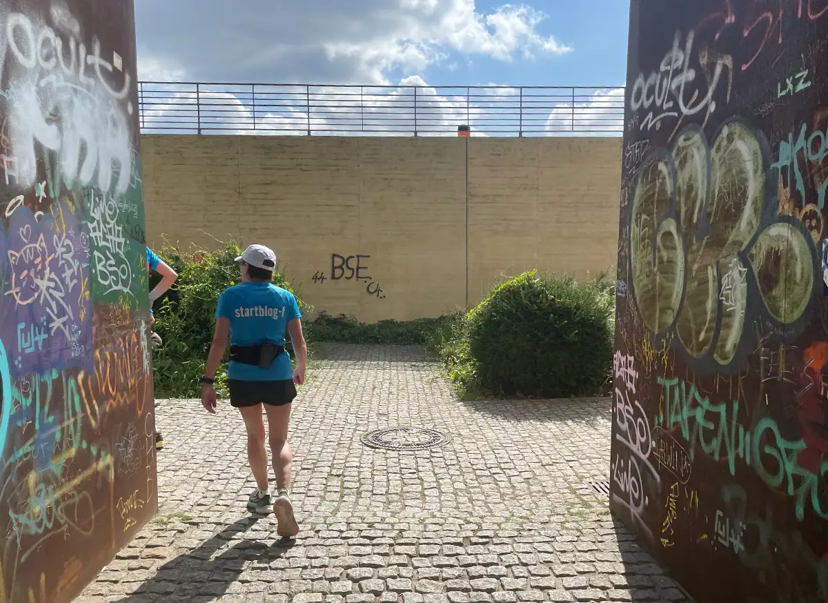 Läuferin in einem schmalen Durchgang zwischen zwei mit Graffitis beschmierten Metallwänden