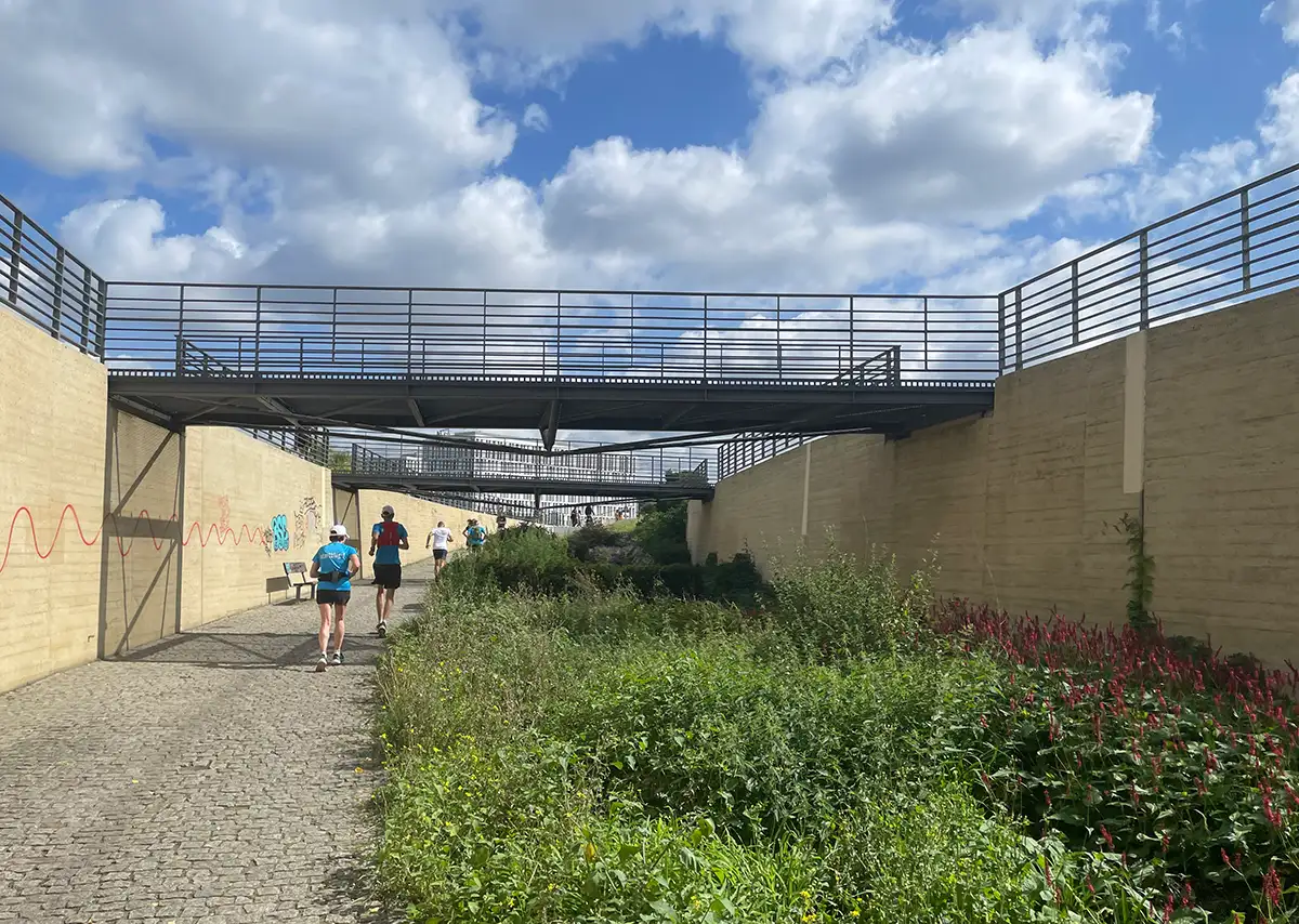 Laufgruppe im Ludwig-Ehrhard-Ufer-Garten, über den mehrere kleine Metallbrücken führen