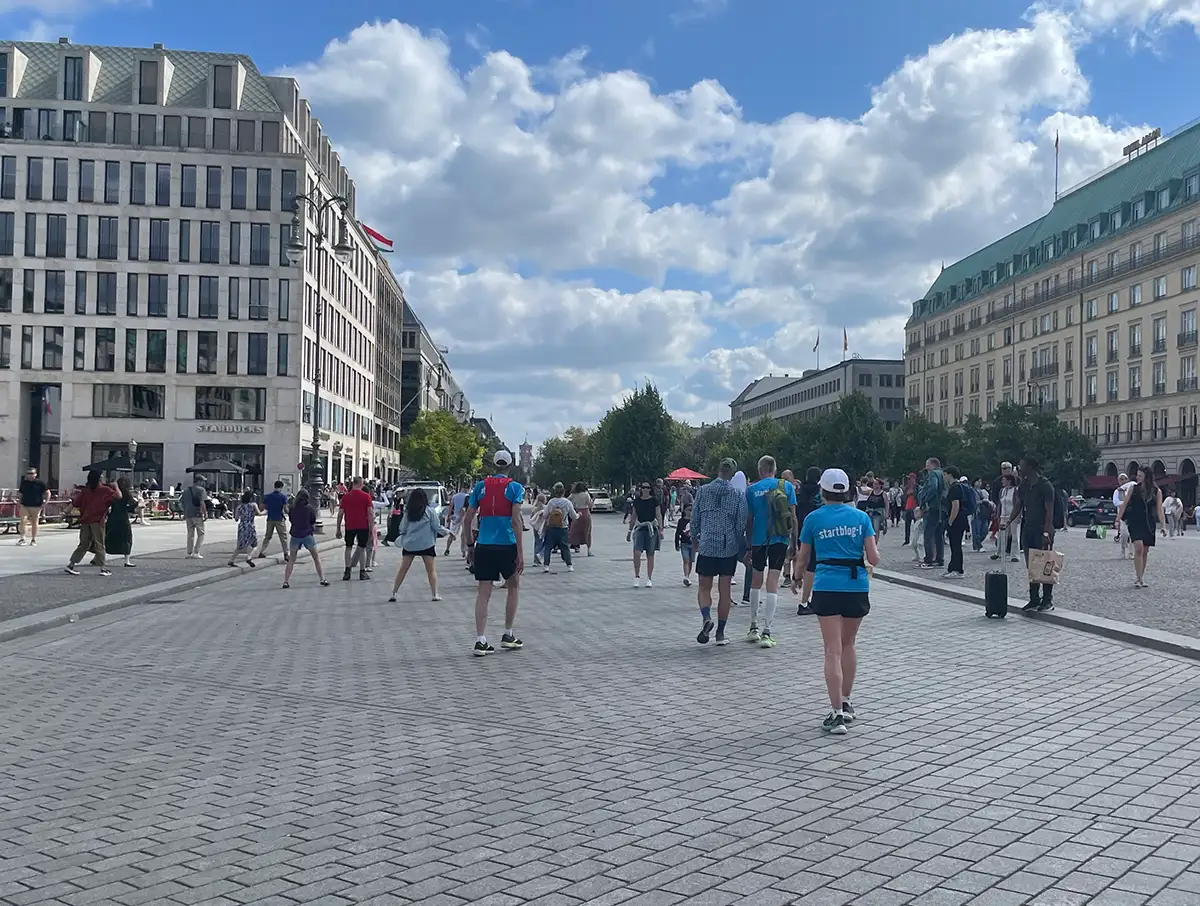 Laufgruppe geht über den Pariser Platz und sieht einer tanzenden Gruppe Menschen zu