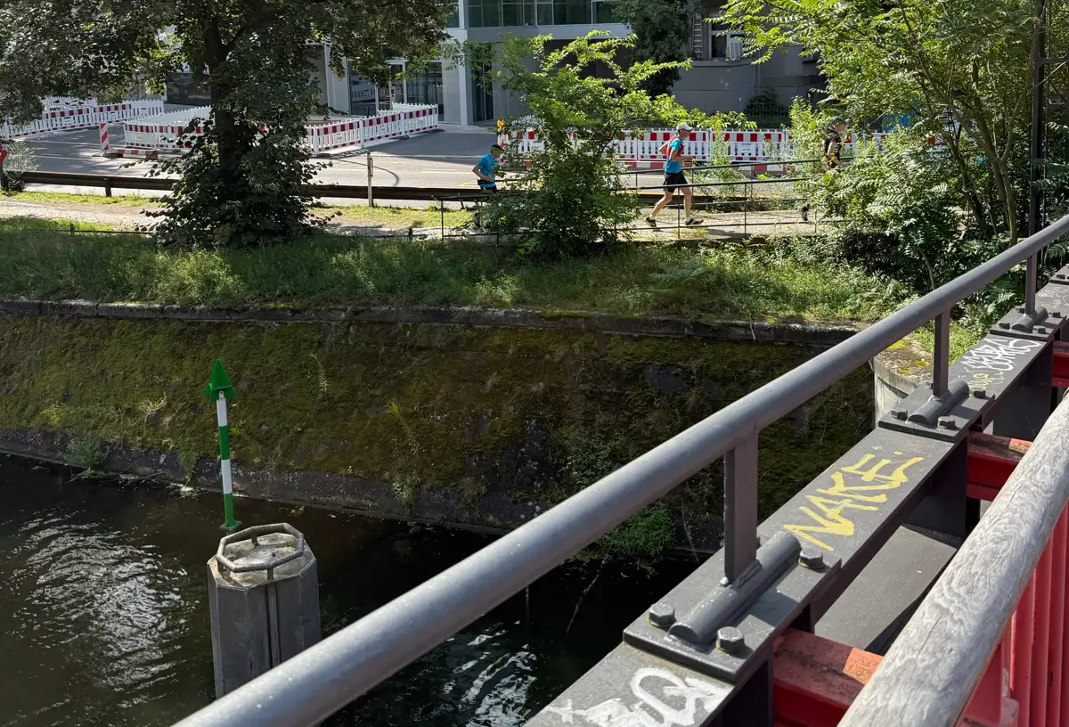 Läufer nähern sich auf dem Uferweg einer Brücke, von der aus man die beiden sieht