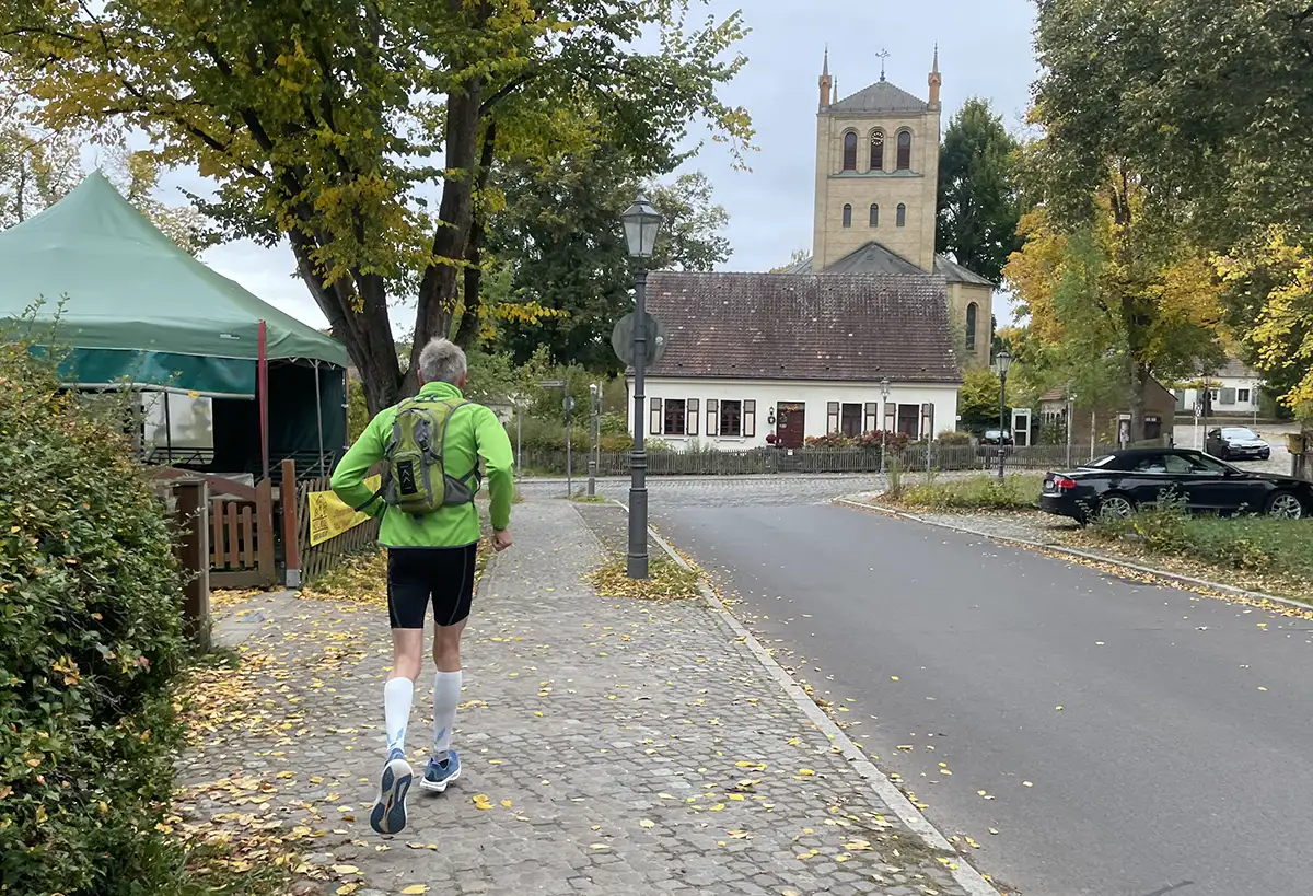 Läufer auf einer Straße, die an einer Kirche mit breitem eckigen Turm endet