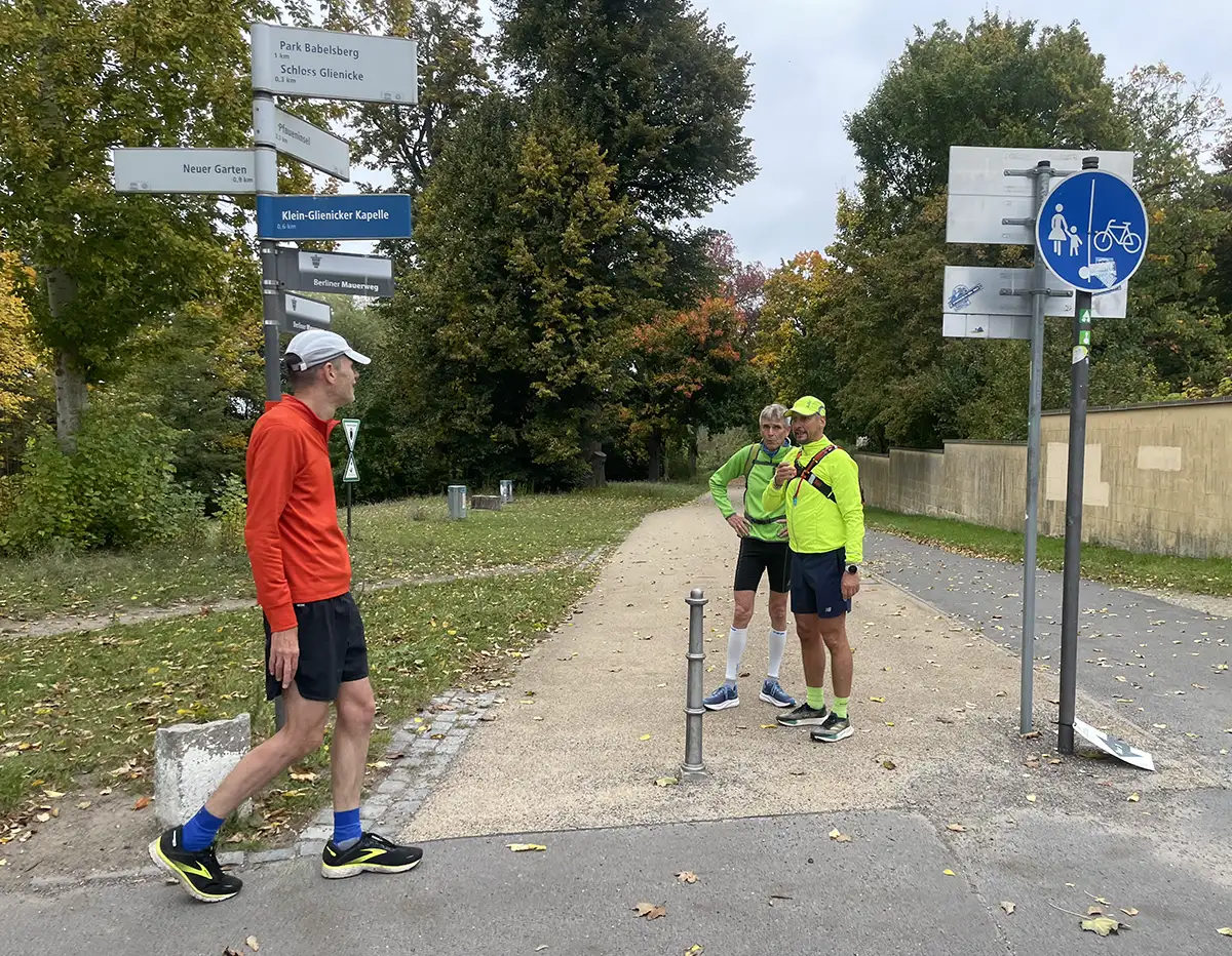Läufer machen Pause neben Pfosten mit vielen Hinweisschildern in alle Richtungen
