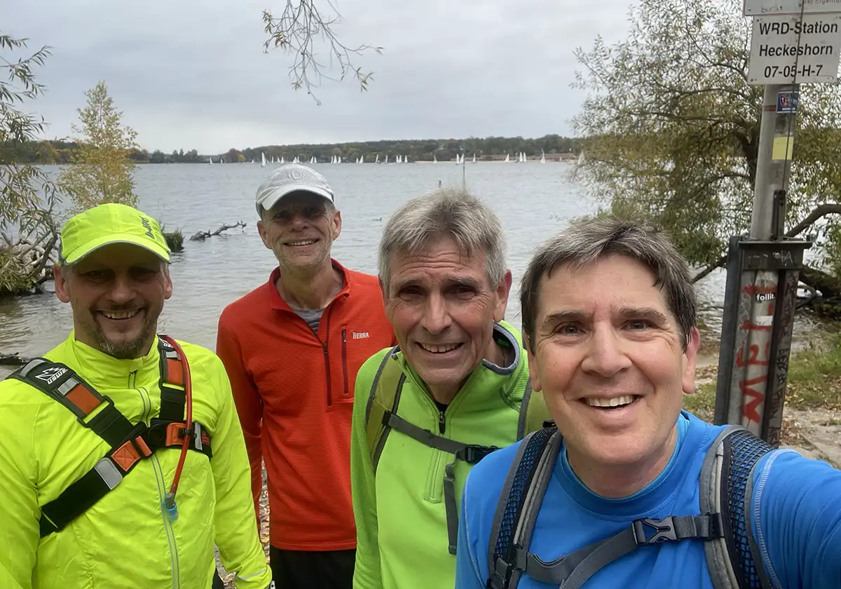 4 Läufer im Gruppenselfie am Ufer, im Hintergrund sind Segelboote zu sehen