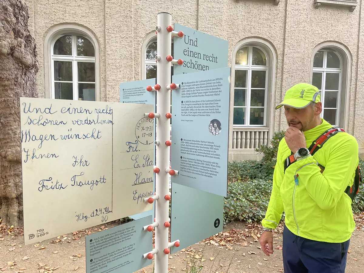 Läufer liest eine Biographie an einer Ausstellungs-Säule vor dem Gebäude