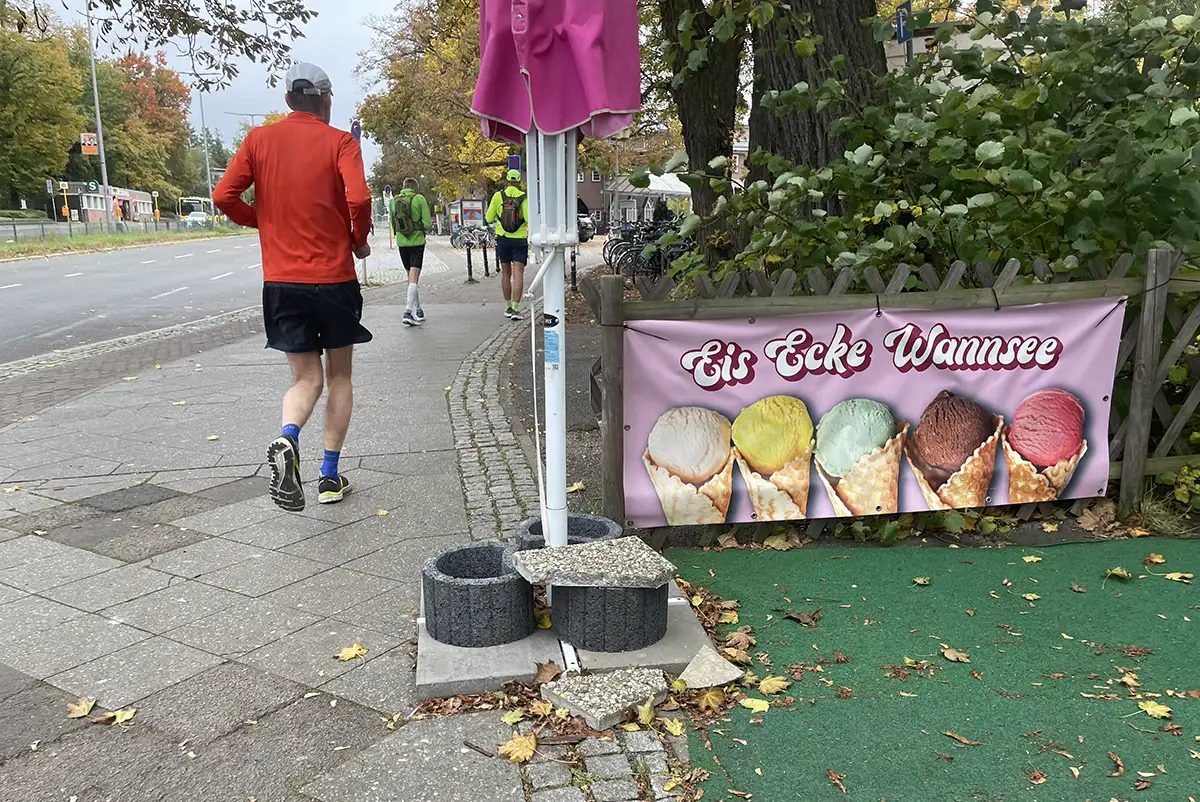 Läufer, daneben ein Banner an einem Holzzaun „Eis Ecke Wannsee“
