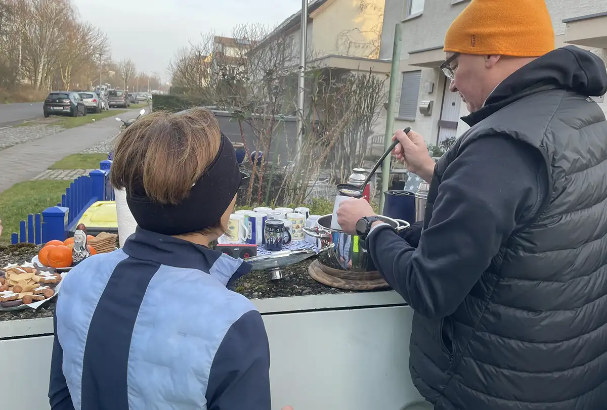 Mann gießt mit Kelle Punsch für eine Läuferin ein