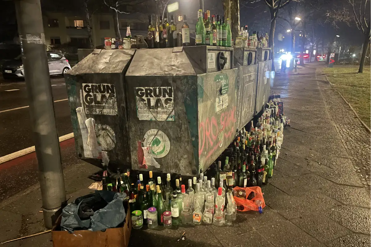 Altglas-Container auf dem und um den herum unzählige leere Flaschen stehen