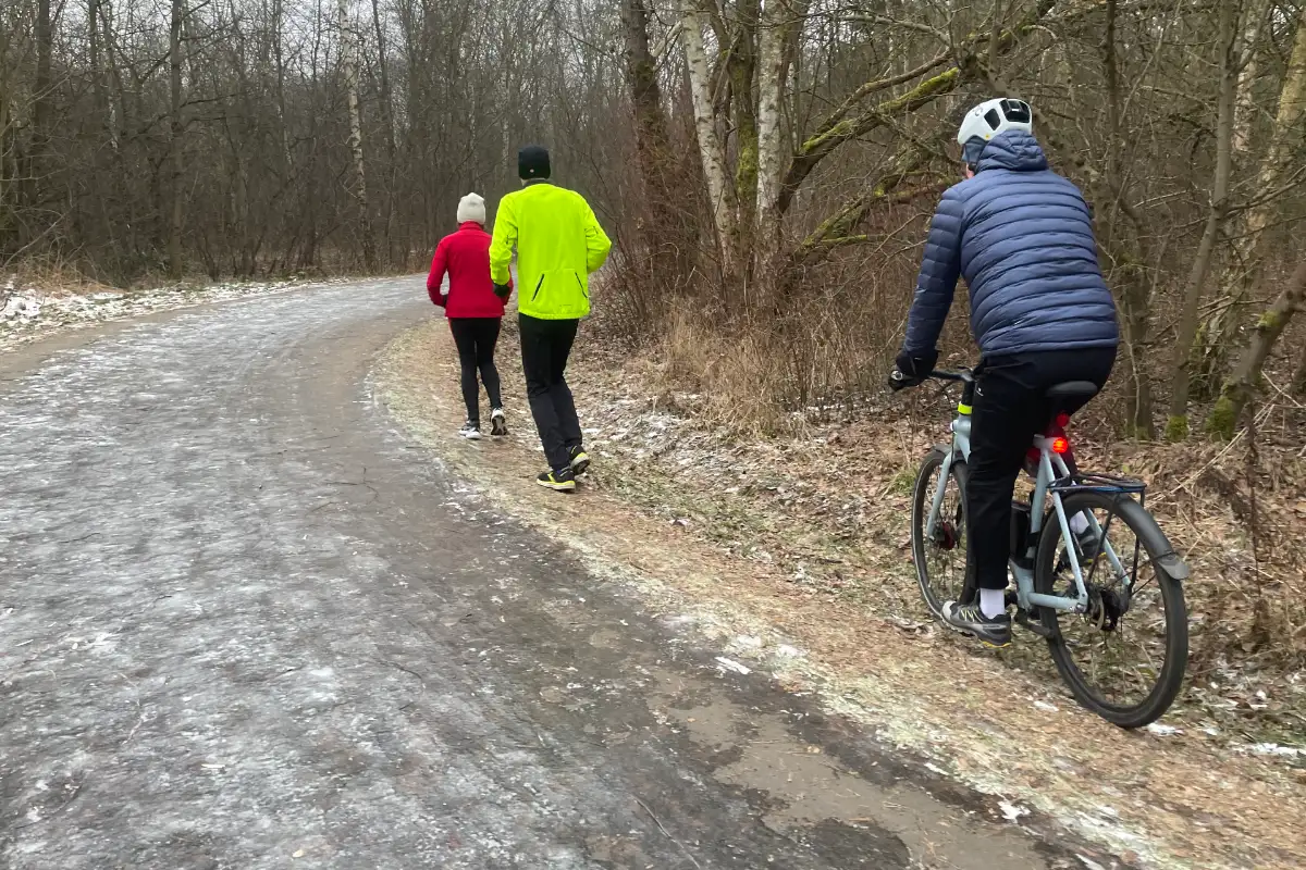 Läuferin, Läufer und Radbegleiter am Rande des eisüberzogenen Asphalts