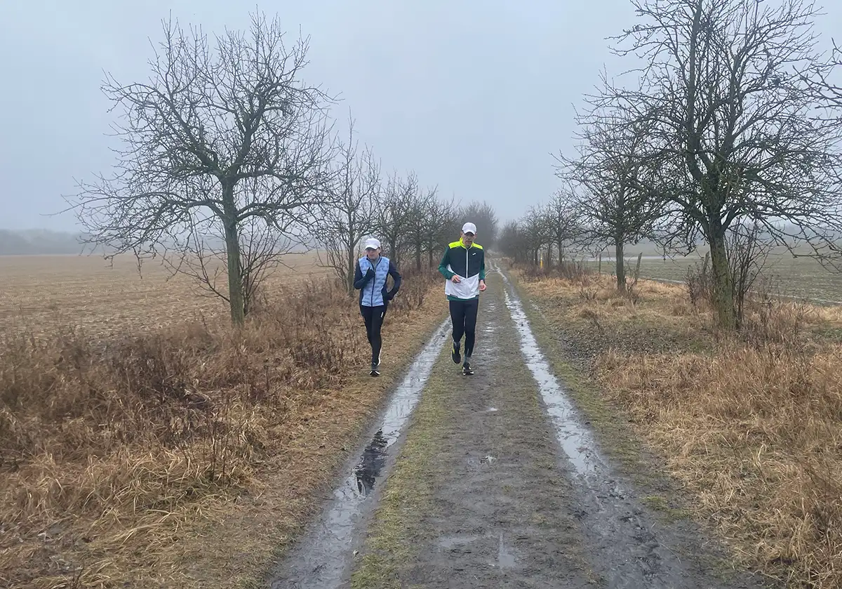 Läuferin und Läufer bei trübem Nieselwetter auf Weg zwichen den Feldern