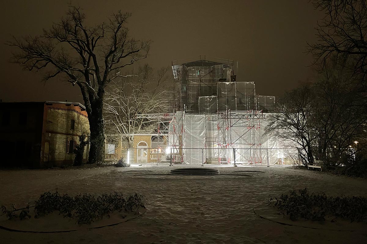 Eingerüstetes, beleuchtetes Gebäude in einem Park im Dunkeln