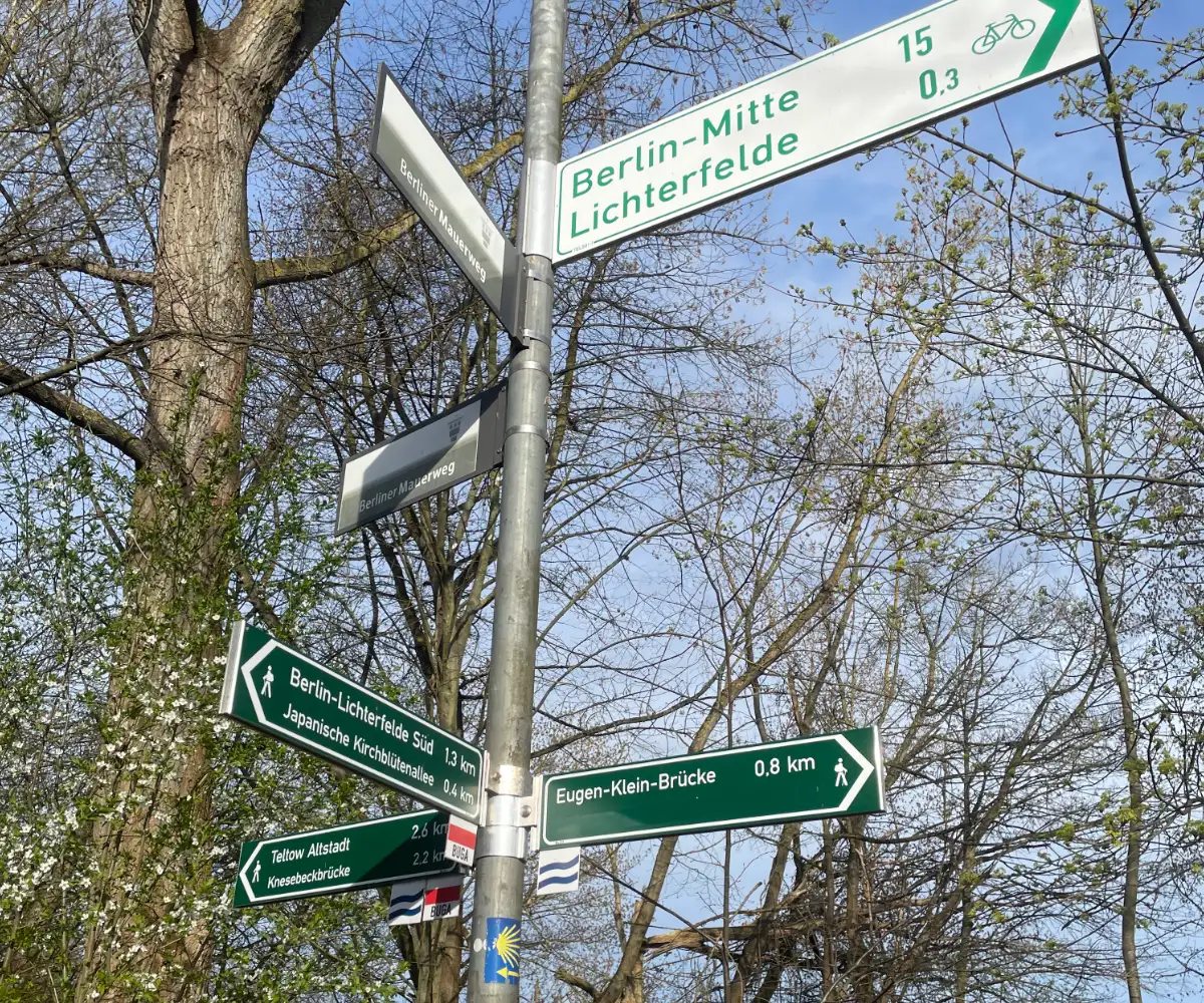 Metallmast mit vielen Richtungs-Schildern: Berlin-Mitte, Lichterfelde, Teltow altstadt, Japanische Kirschblütenallee, Eugen-Klein-Brücke, etc.