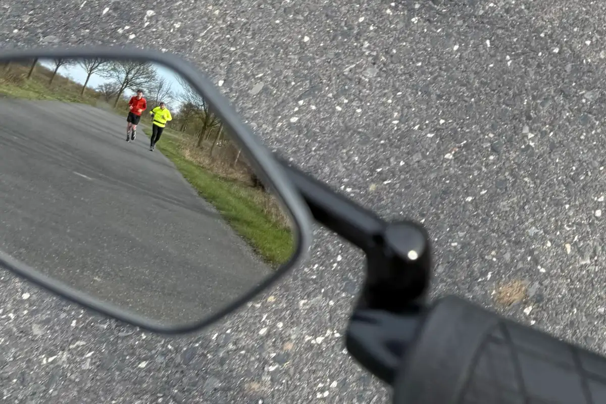 Im Rückspiegel des Fahrrads sind die beiden Läufer zu erkennen