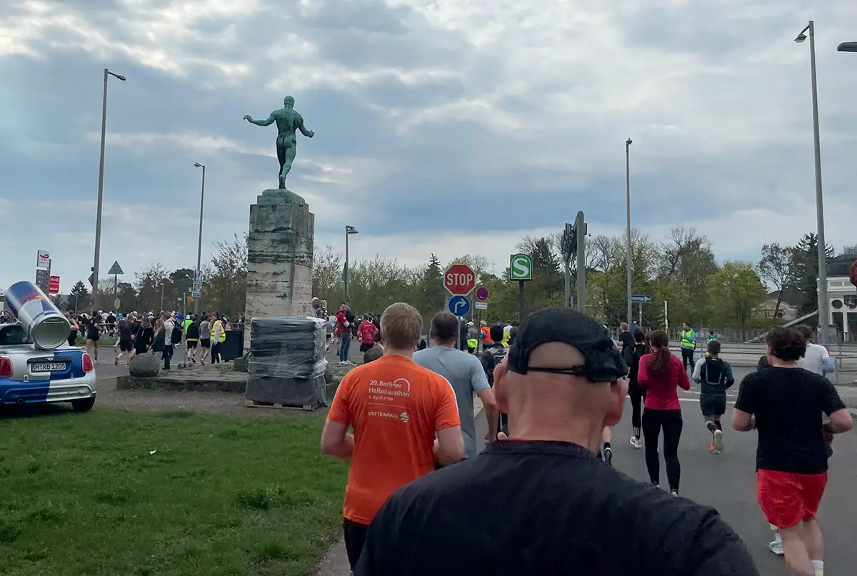 Läufer laufen einen Bogen um eine Statue auf einem hohen Sockel