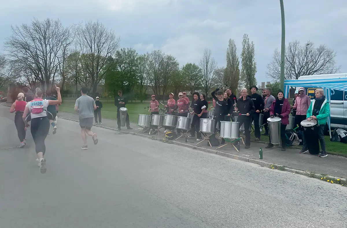 Trommelgruppe mit silbernen Trommeln, eine Läuferin winkt ihnen zu