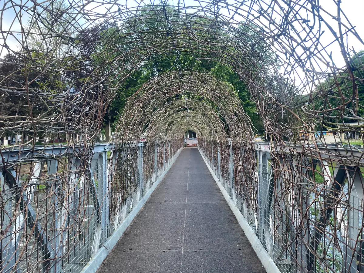 Fußgängerbrücke, überspannt von Rankgittern mit noch blattlosen Zweigen