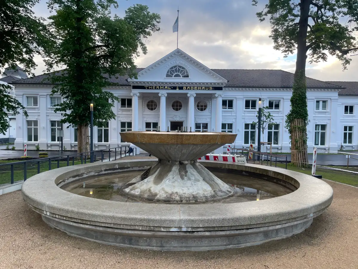 Weißes, historisches Thermal-Badehaus mit noch inaktivem Springbrunnen davor