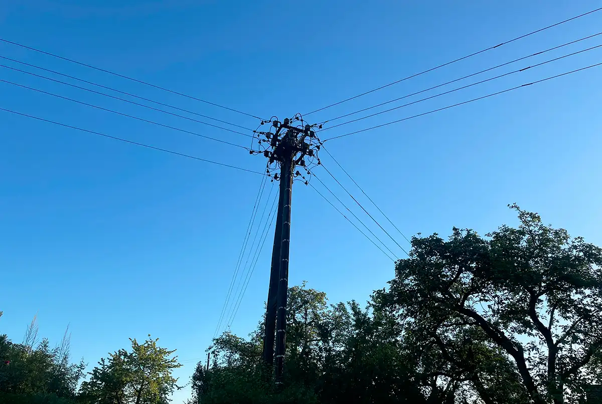 Strommast vor blauem Himmel, von dem jeweils 4 Kabel in 4 Richtungen abgehen