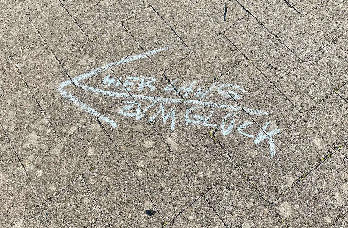 Pfeil mit Kreideschrift auf dem Pflasterweg „Hier lang zum Glück“