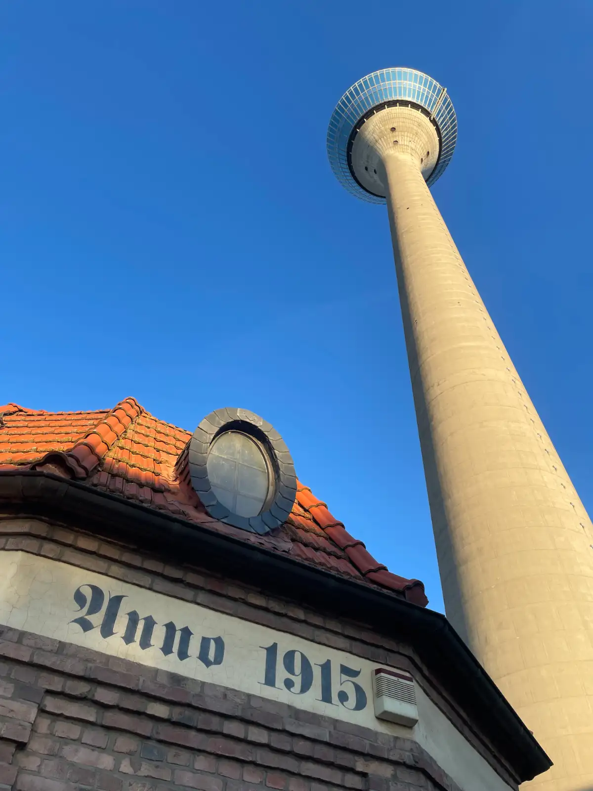 Blick hinauf zum Rheinturm, im Vordergrund ein altes Gebäude mit Aufschrift Anno 1915