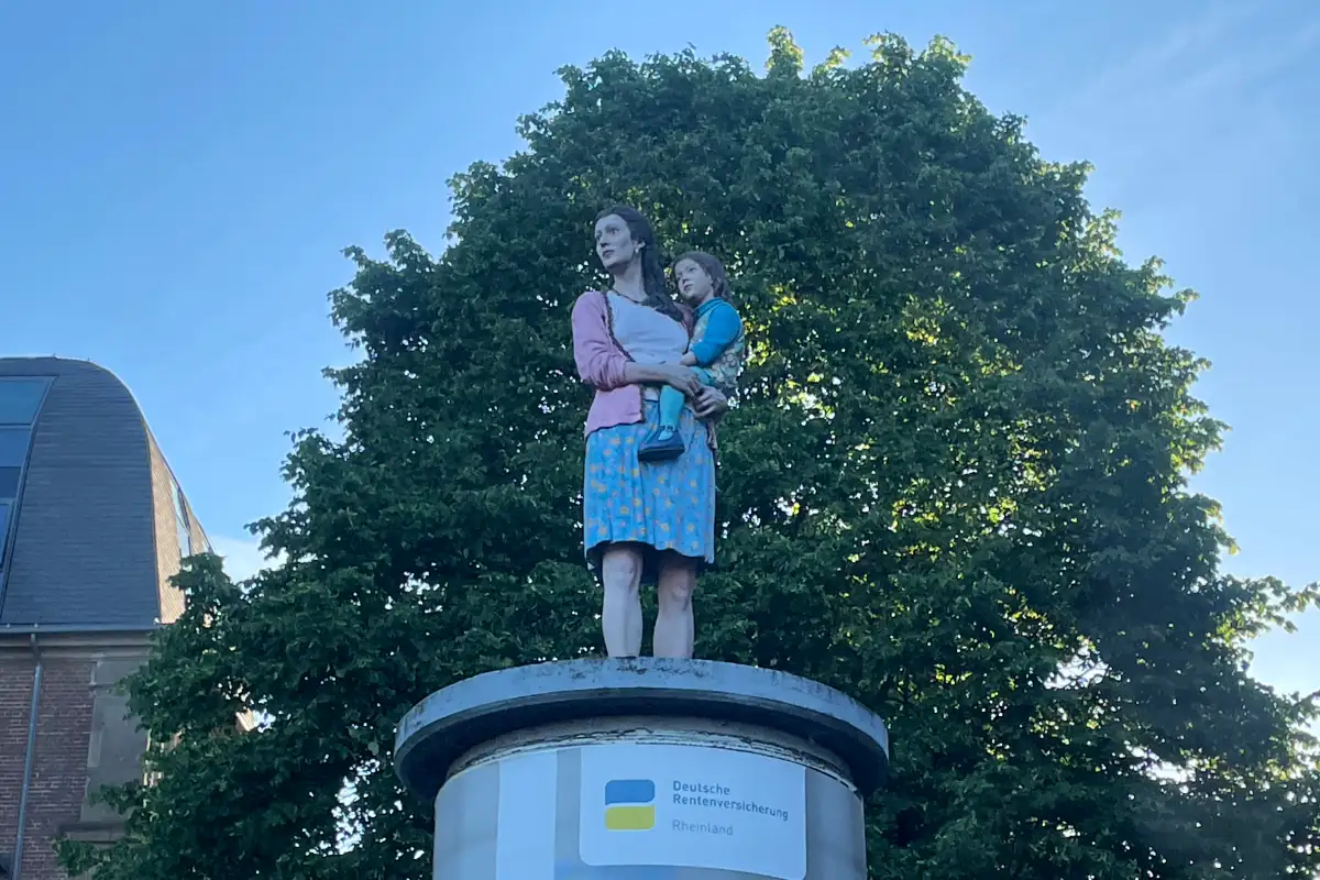 Lebensgroße Figur einer Frau mit einem Kind auf dem Arm auf einer Litfaßsäule
