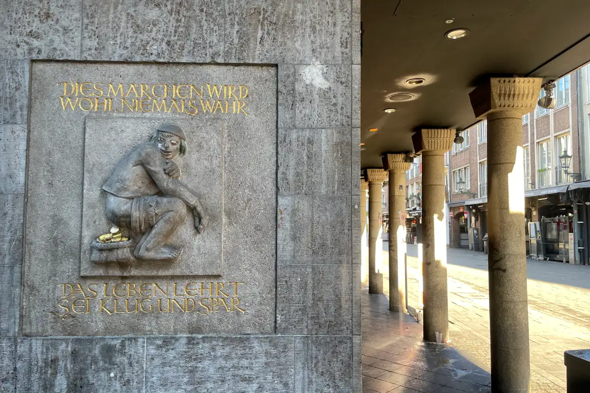 Relief an einer Mauer mit einem Mann, der Goldstücke scheißt. Dazu der Spruch: Dies Märchen wird wohl niemals wahr, das Leben lehrt sei klug und spar