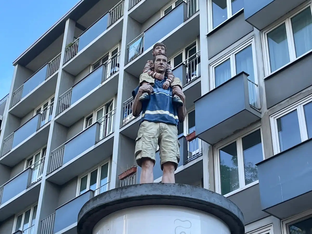 Lebensgroße Figur eines Vaters mit seinem Sohn auf den Schultern auf einer Litfaßsäule