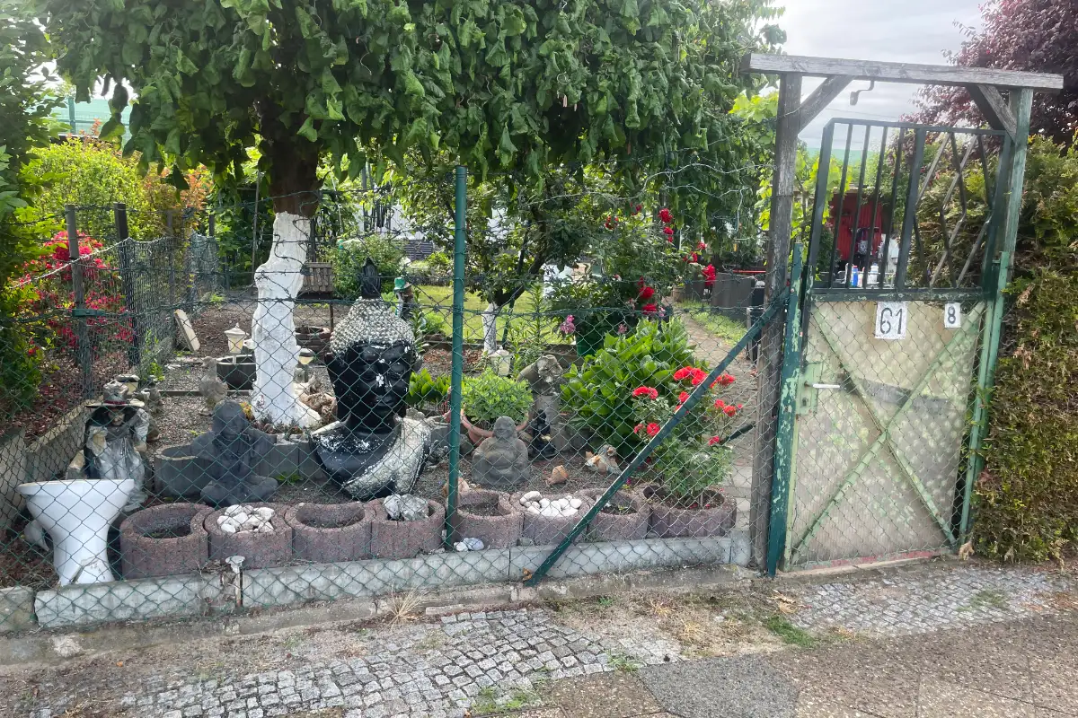 Kleingarten mit diversen Figuren am Zaun: Hexe und Buddha