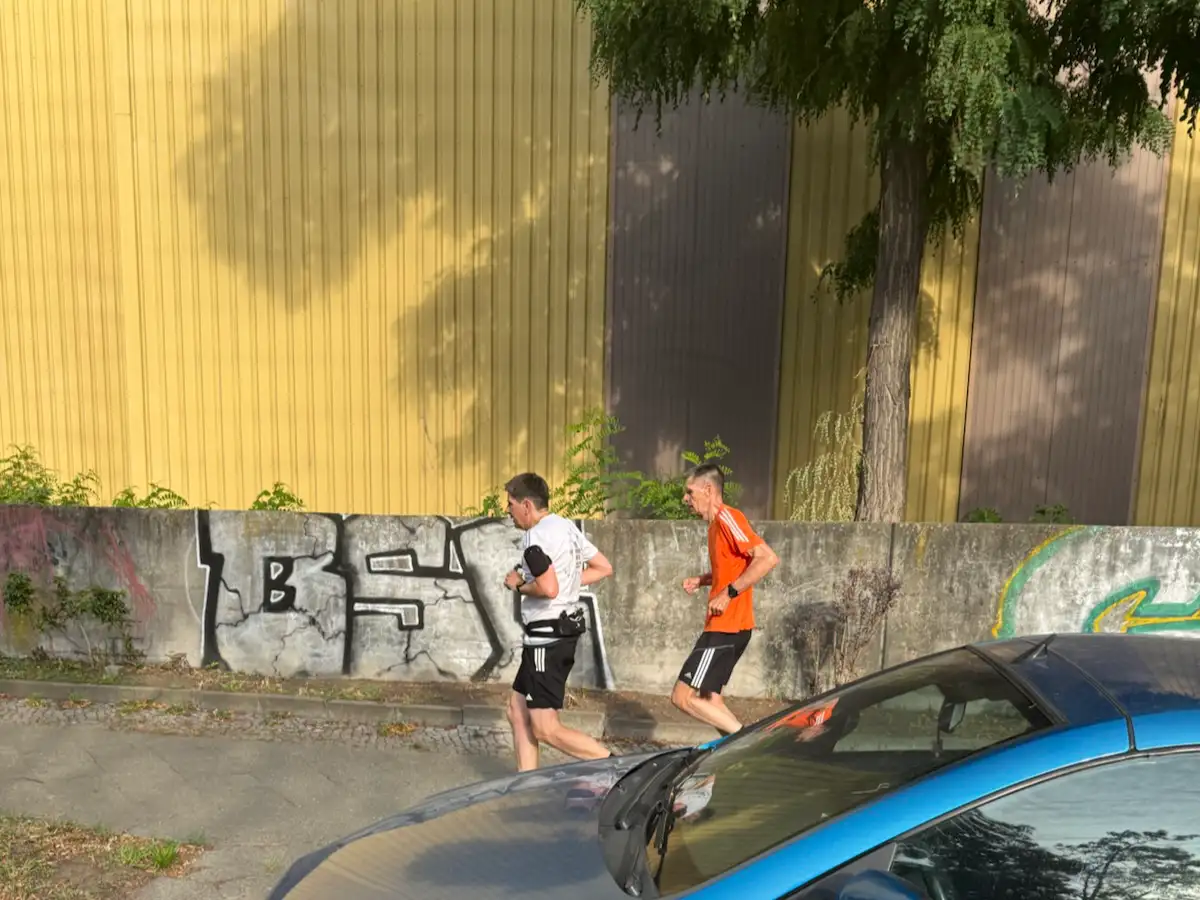 Zwei Läufer vor einer hohen gelben Industriehalle