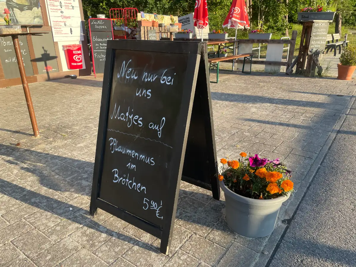 Schild vor einer Gaststätte „Neu nur bei uns: Matjes auf Pflaumenmus im Brötchen“