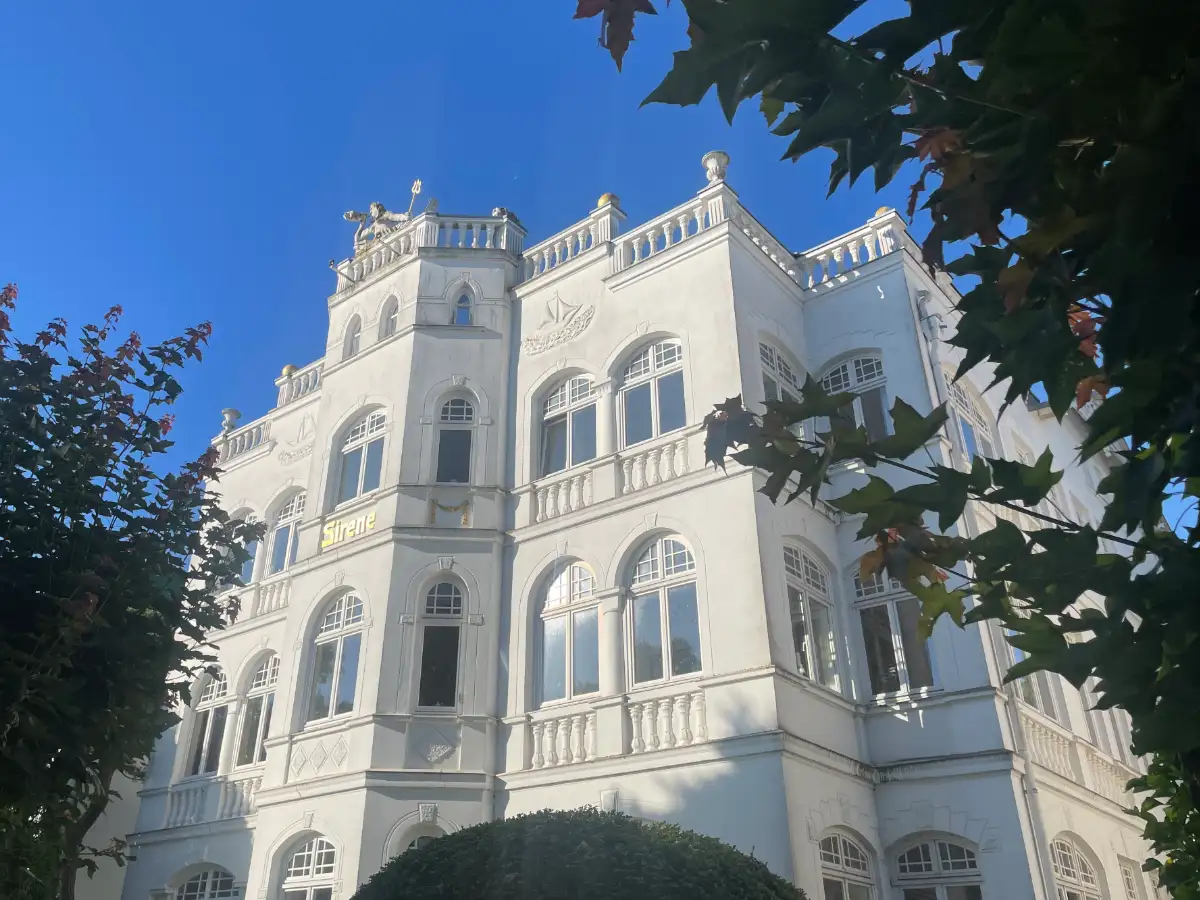 Weiße Villa „Sirene“ mit Meeresgott-Skulptur hinter einer Balustrade auf dem Dach
