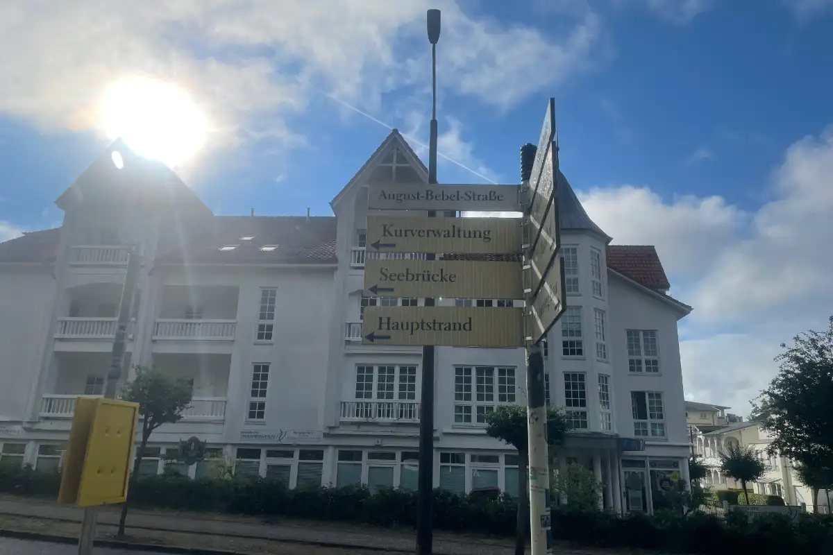 Weißes Gebäude, davor Wegweiser zur Kurverwaltung und zur Seebrücke