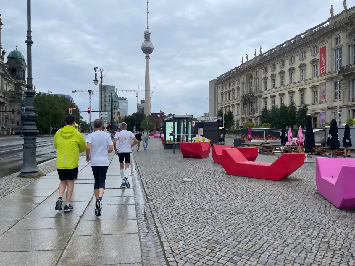 Laufgruppe neben dem Humboldt-Forum, vor dem rote und rosafarbene moderne Sitzelemente liegen