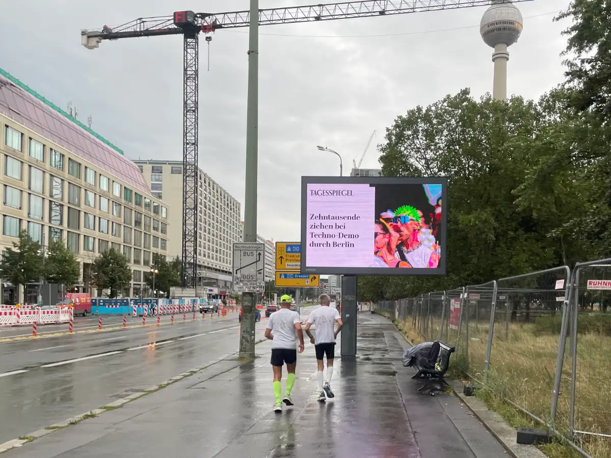 Läufer auf breiter Straße mit Digitaltafel, dahinter der Fernsehturm
