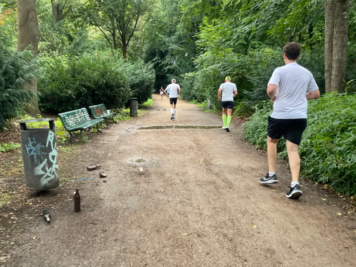 Laufgruppe auf Parkweg mit leeren Bierflaschen neben einem Mülleimer