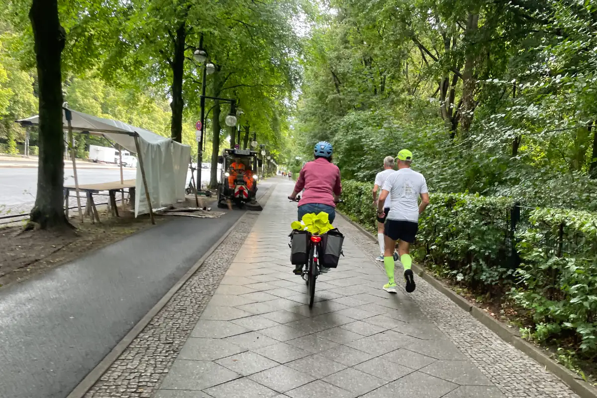 2 Läufer mit Radbegleiterin auf einem Fußweg neben dem Tiergarten
